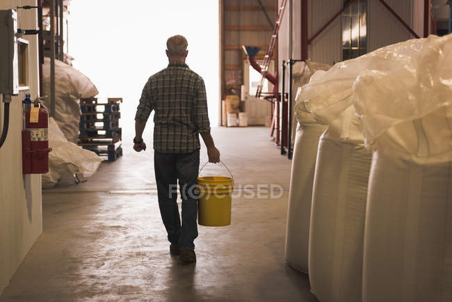 Visão traseira do homem carregando com balde cheio de grãos na fábrica — Fotografia de Stock