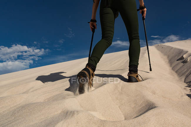 Low section of female hiker with trekking pole walking on sand — Stock Photo