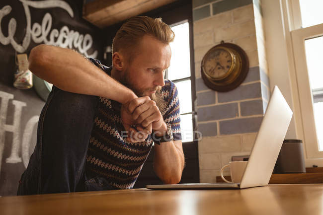 Чоловік сидить на столі і дивиться на свій ноутбук на кухні — стокове фото