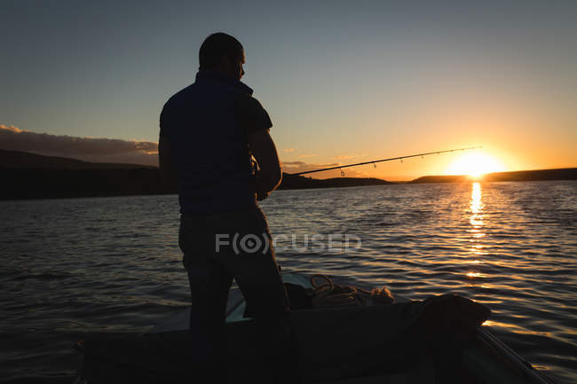 Man fishing while standing on motorboat in river at sunset. — Stock Photo