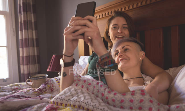 Lesbian couple taking selfie in bed at home. — Stock Photo