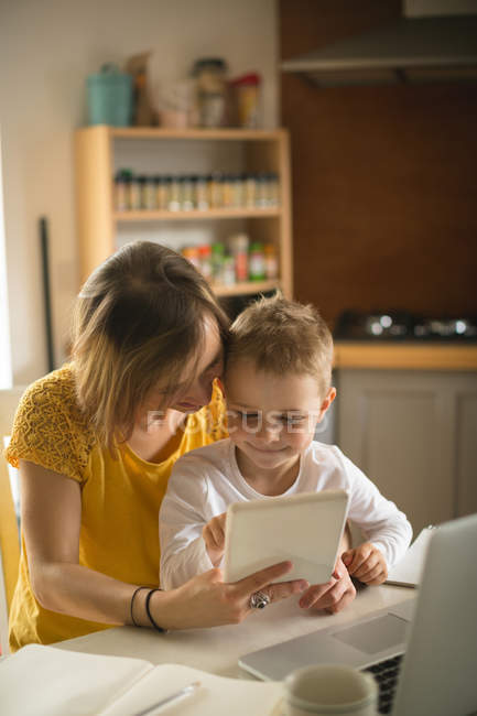 Mother with son sitting on chair using digital tablet in kitchen at home — Stock Photo