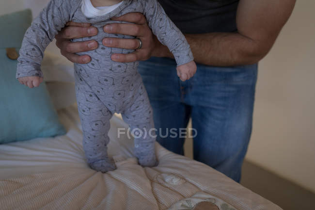 Partie médiane du père tenant bébé garçon sur le lit à la maison
. — Photo de stock