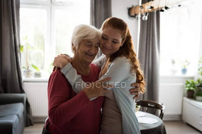Улыбающиеся бабушка и внучка обнимают друг друга в гостиной — стоковое фото