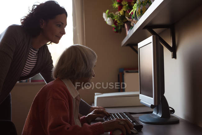 Доглядач допомагає старшій жінці під час роботи на комп'ютері в кімнаті для престарілих — стокове фото