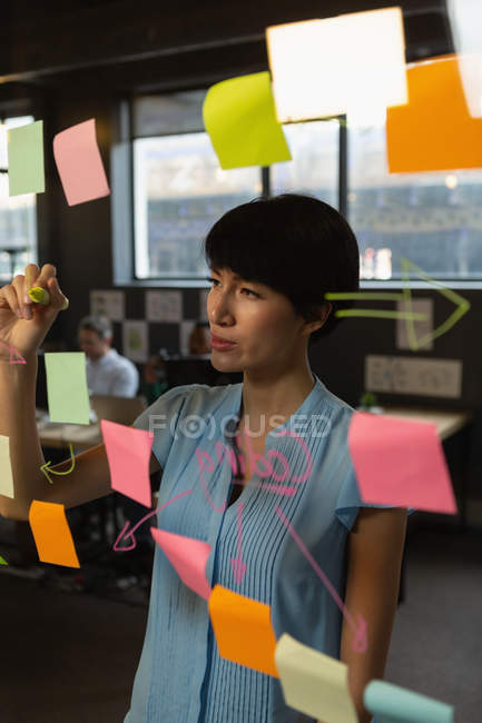 Female executive writing notes on glass wall in office. — Stock Photo