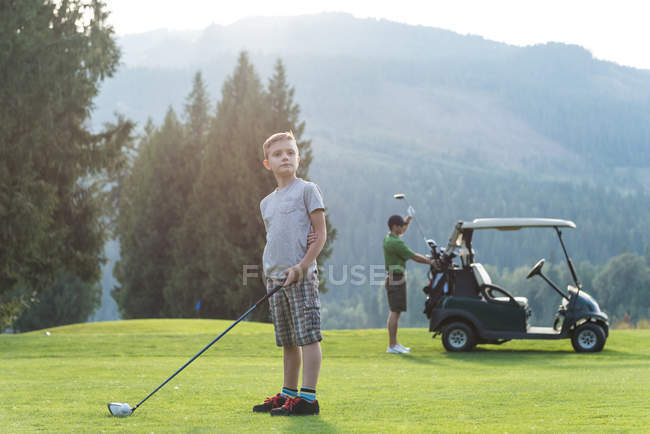 Задумчивый мальчик стоит с клюшкой для гольфа на поле — стоковое фото