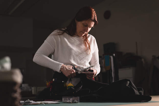 Tailor cutting clothes with scissors at workshop — Stock Photo