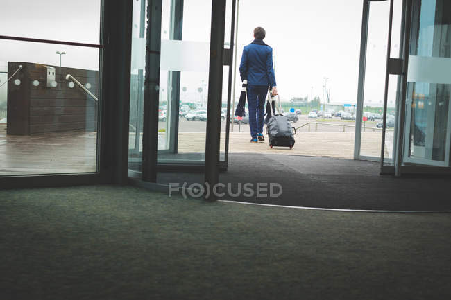 Вид ззаду бізнесмена, що виходить з готелю з багажем — стокове фото
