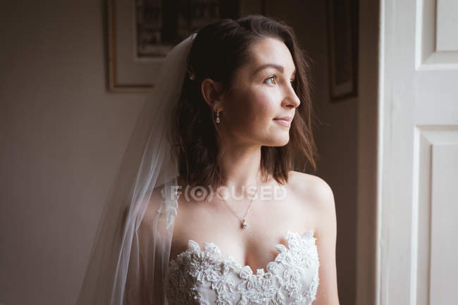 Улыбающаяся невеста смотрит в окно дома — стоковое фото