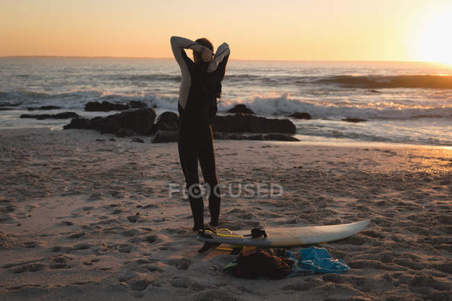 Vista posteriore del surfista in piedi sulla spiaggia durante il tramonto — Foto stock