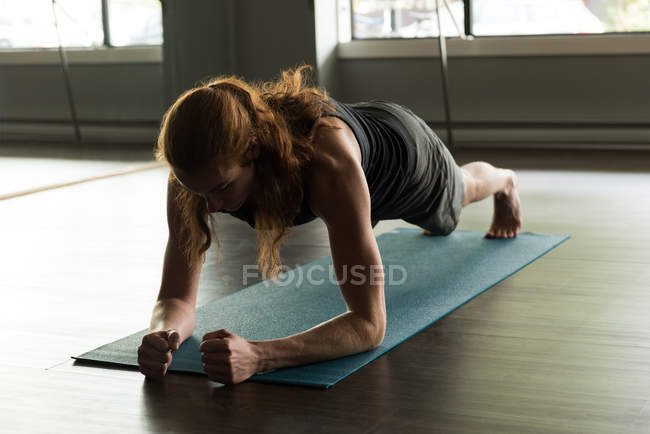 Jeune homme aux longs cheveux roux faisant de l'exercice de planche dans un studio de fitness . — Photo de stock