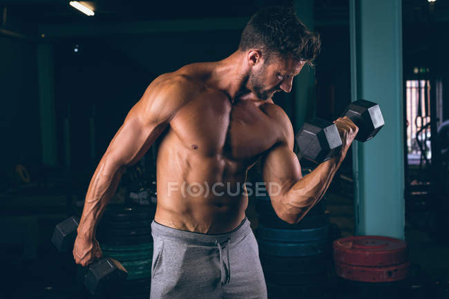 М'язистий чоловік займається з гантелями в фітнес-студії — стокове фото