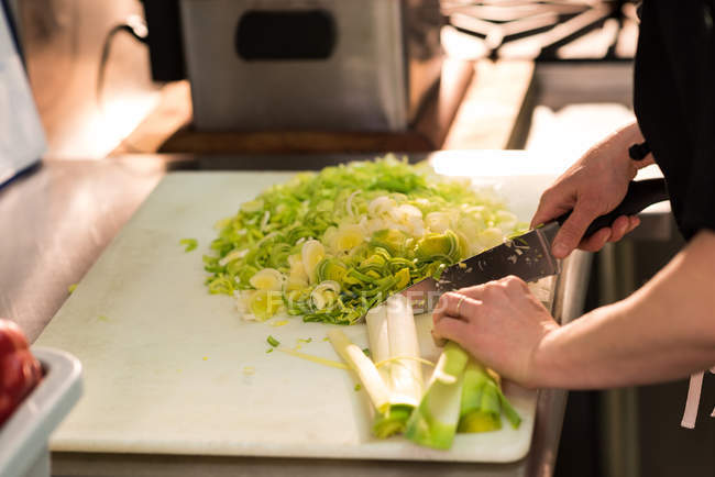 Seção intermediária de chef cortando vegetais em uma cozinha comercial — Fotografia de Stock
