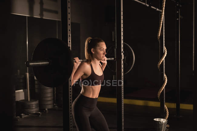 Jeune femme levant avec haltère dans la salle de gym — Photo de stock