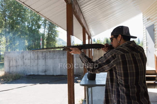 Vista laterale dell'uomo che punta il fucile al bersaglio nel poligono di tiro — Foto stock