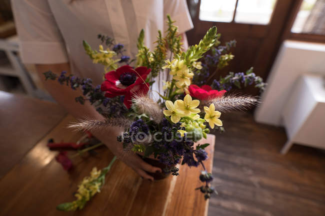 Средняя часть женщины, держащей вазу с цветами дома — стоковое фото
