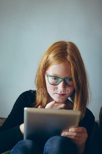 Menina inteligente em óculos usando tablet digital em casa — Fotografia de Stock