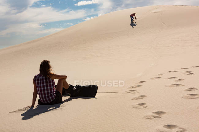 Frau sucht Mann beim Sandboarding in der Wüste an einem sonnigen Tag — Stockfoto