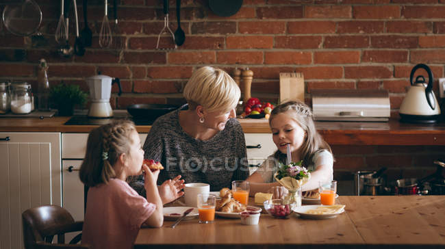 Mère et les enfants prennent le petit déjeuner à table dans la cuisine — Photo de stock