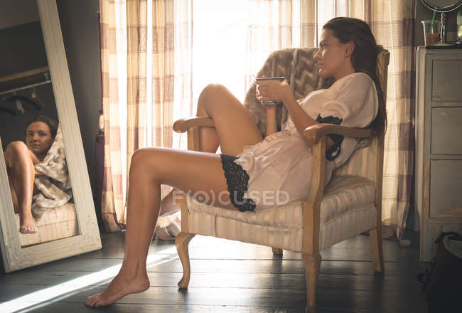 Mujer sentada en la silla mientras toma café en casa
. - foto de stock
