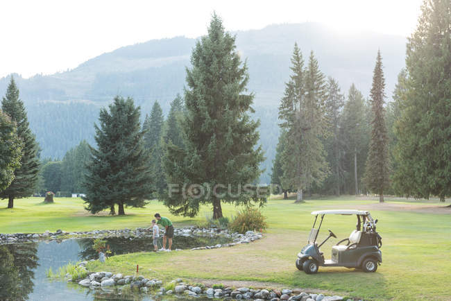 Отец и сын стоят у пруда на поле для гольфа — стоковое фото