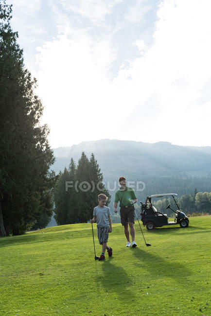 Padre e hijo caminando con el club de golf en el campo - foto de stock