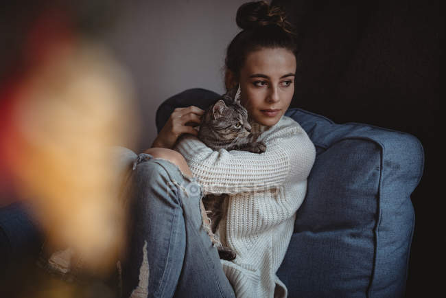 Mujer abrazando a su gato mascota en el sillón en casa - foto de stock
