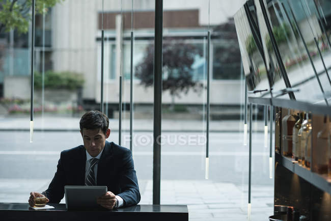 Бізнесмен використовує цифровий планшет, маючи віскі на стійці для готелів — стокове фото