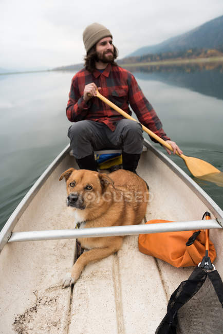 Uomo remo canoa nel fiume con il suo cane a bordo — Foto stock