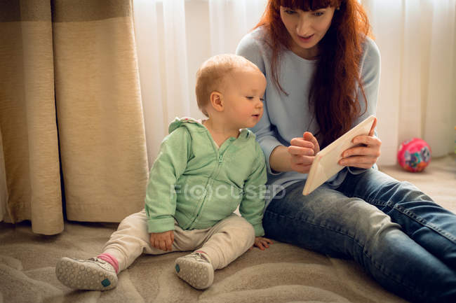 Мама показывает своей малышке цифровой планшет дома — стоковое фото