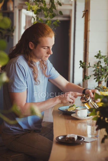 Mann schüttet Kaffee in Tasse an Tisch in Café — Stockfoto