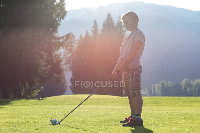 Vista lateral del chico golpeando tiro de golf en el campo - foto de stock