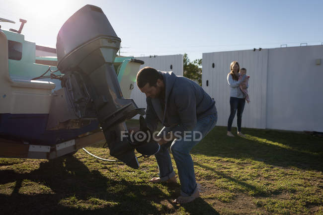 Man repairing motor boat in backyard with family in background. — Stock Photo