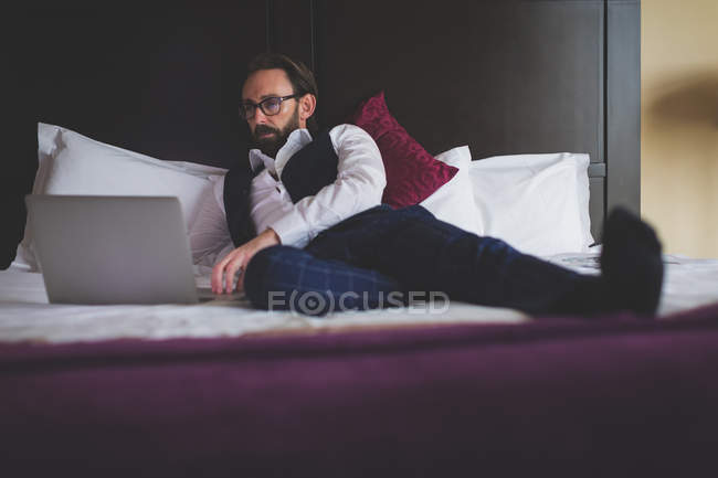 Homme d'affaires utilisant un ordinateur portable sur le lit de l'hôtel — Photo de stock