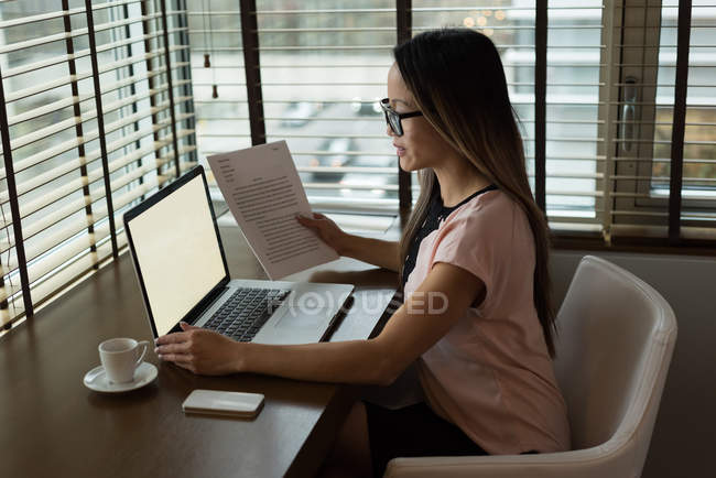 Empresária vestindo óculos trabalhando em seu laptop no escritório — Fotografia de Stock