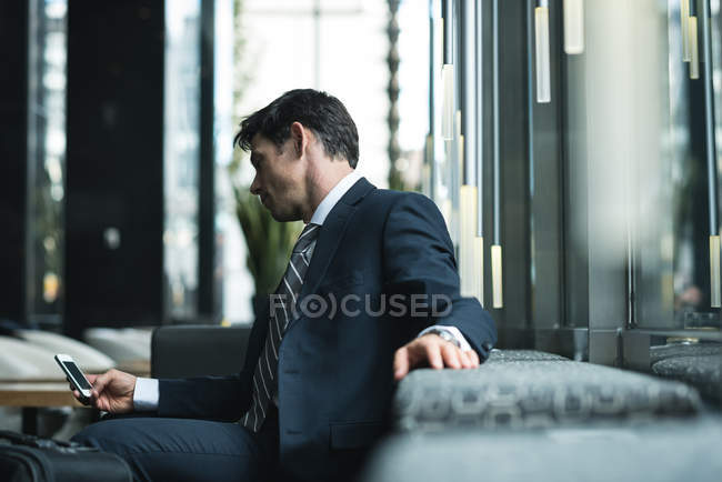 Uomo d'affari che utilizza il telefono cellulare nella hall dell'hotel — Foto stock