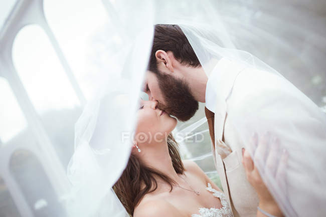 Nahaufnahme von Braut und Bräutigam, die sich unter dem Schleier küssen — Stockfoto