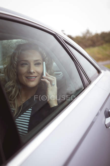 Усміхнена бізнес-леді розмовляє по телефону на задньому сидінні автомобіля — стокове фото