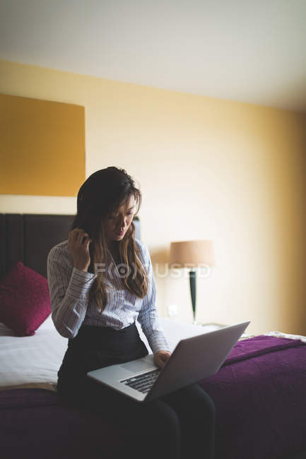 Femme d'affaires utilisant un ordinateur portable sur le lit dans la chambre d'hôtel — Photo de stock