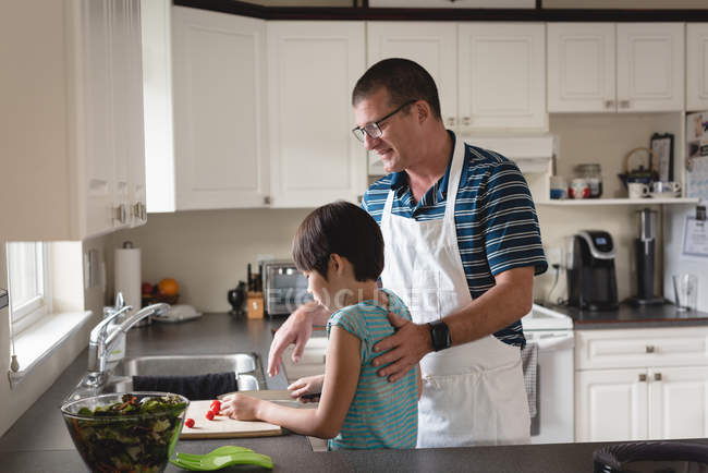 Attentif père aider son fils à couper des légumes dans la cuisine — Photo de stock