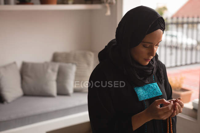 Mujer musulmana rezando con cuentas de oración en casa - foto de stock