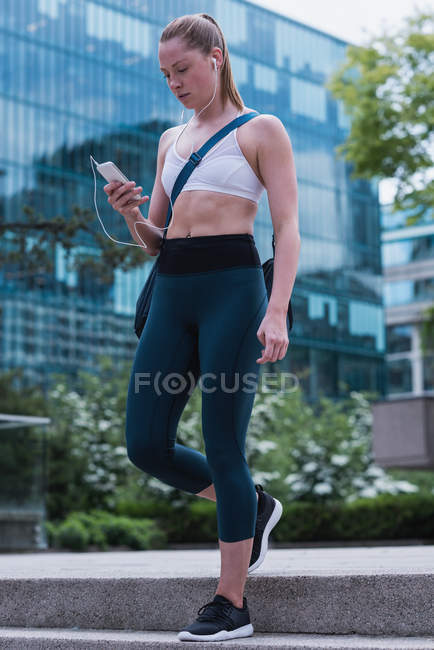 Jovem mulher esportiva usando telefone celular na rua — Fotografia de Stock