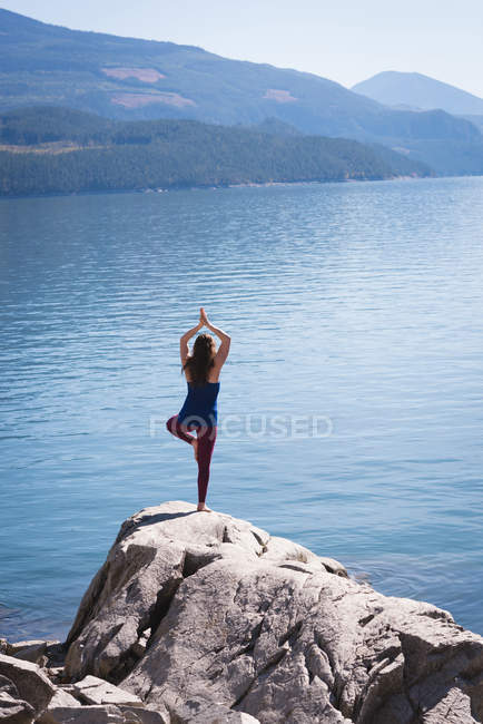 Женщина практикует йогу на скале возле моря — стоковое фото