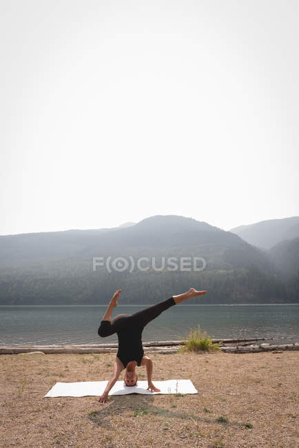 Sporty woman practicing head stand near the sea coast on a sunny day — Stock Photo