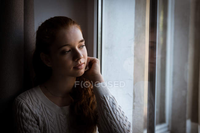 Задумчивая девочка-подросток смотрит в окно дома — стоковое фото