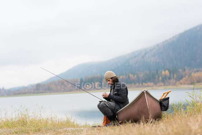 Человек, сидящий на лодке возле реки со своим рыболовецким снаряжением — стоковое фото