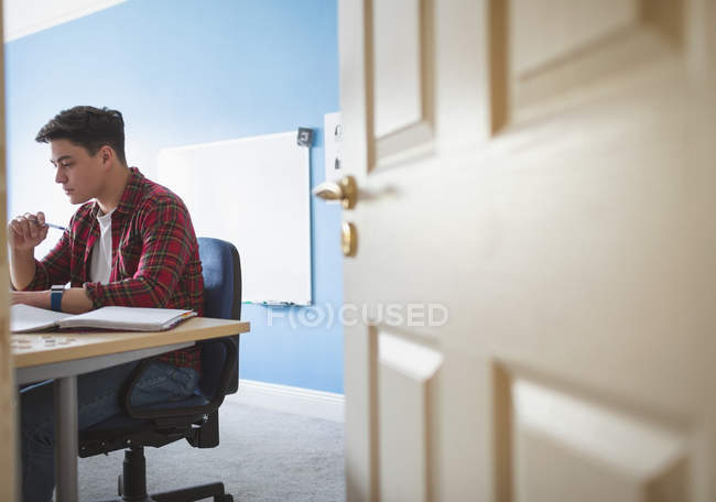Hombre joven estudiando en la habitación, vista detrás de la puerta . - foto de stock