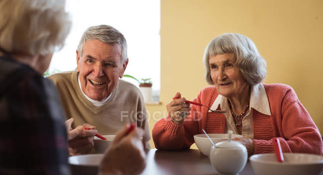 Улыбающиеся старшие друзья, общающиеся за завтраком в доме престарелых — стоковое фото