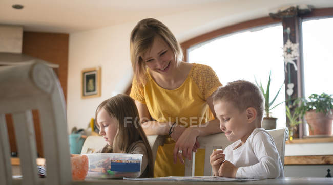 Mère aidant les enfants avec des devoirs dans la cuisine à la maison — Photo de stock